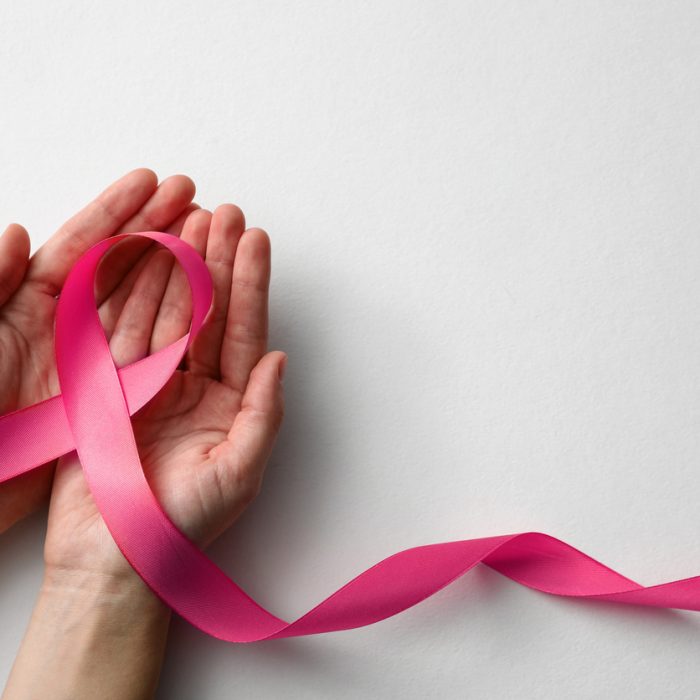 Woman holding pink ribbon on white background, top view with space for text. Breast cancer awareness concept